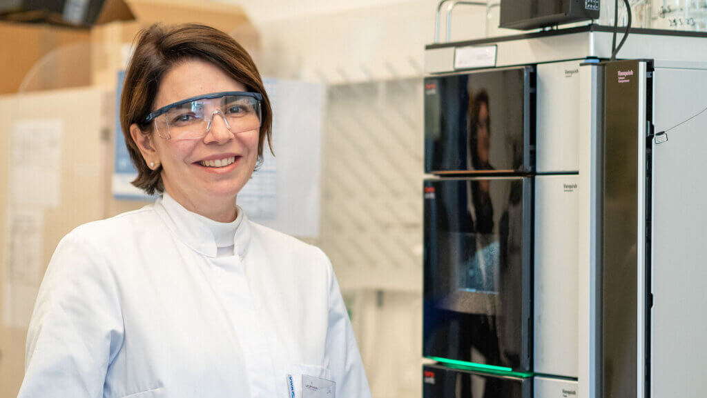 Retrato da professora Vania Zuin. Ela veste branco e óculos trasparentes, remetendo a um laboratório de química. A professora é branca, tem cabelos curtos e castanhos e está sorrindo na foto.
