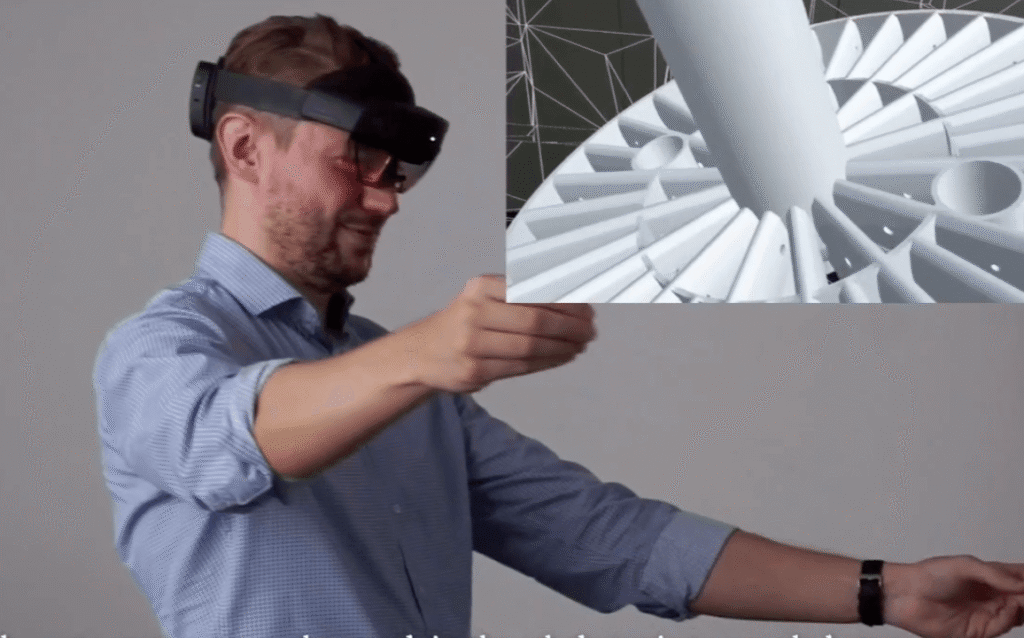 A imagem mostra um pesquisador usando óculos tecnológicos enquanto mexe os braços, que, com isso, alteram uma imagem de projeto.